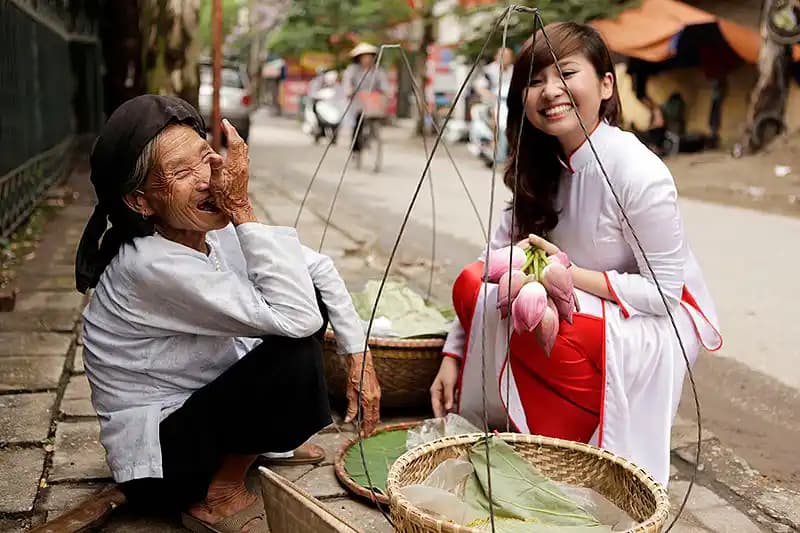 Vietnamese girl in ao dai and old lady merchant